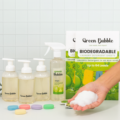 Green Bubble eco-friendly laundry products including bottles, a box of detergent sheets, and a hand holding detergent pods on a tiled background.