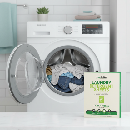 White washing machine with open door showing clothes inside, next to a box of green bubble laundry detergent sheets.